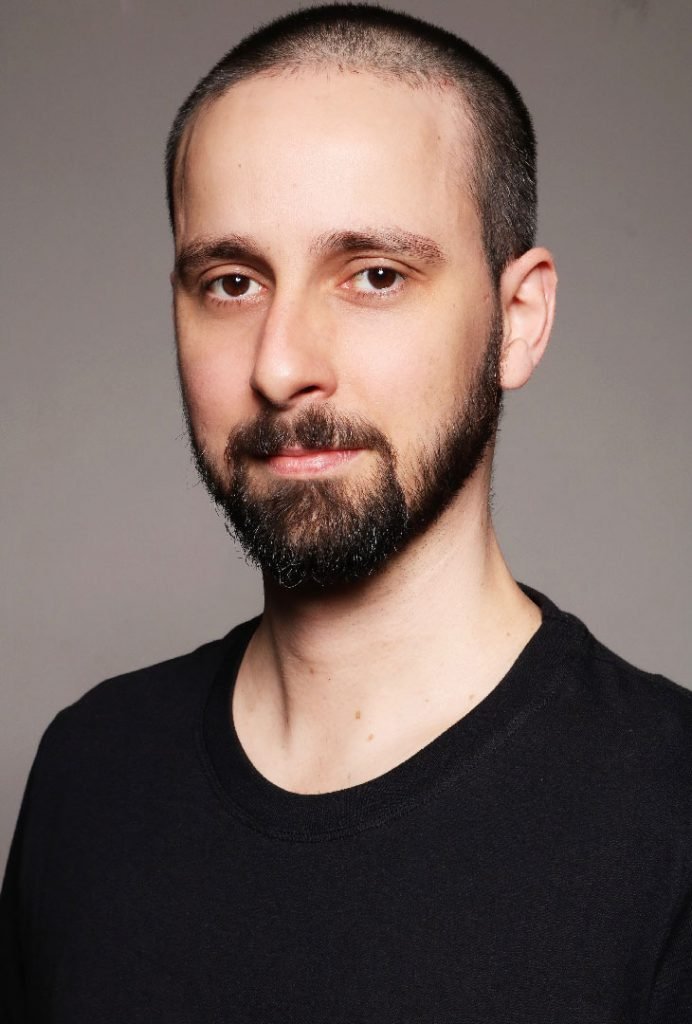 Retrato de Rafael Érnica em close, de camiseta preta, olhando diretamente para a câmera com expressão neutra.